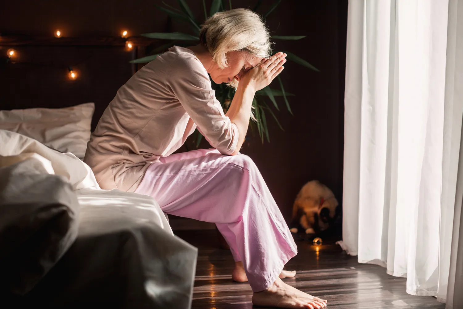 Frauenarztpraxis Dr. A. Dietrich - Gesundheitsdienste für Frauen - Eine Person im rosa Pyjama sitzt auf der Bettkante und stützt den Kopf in die Hände.