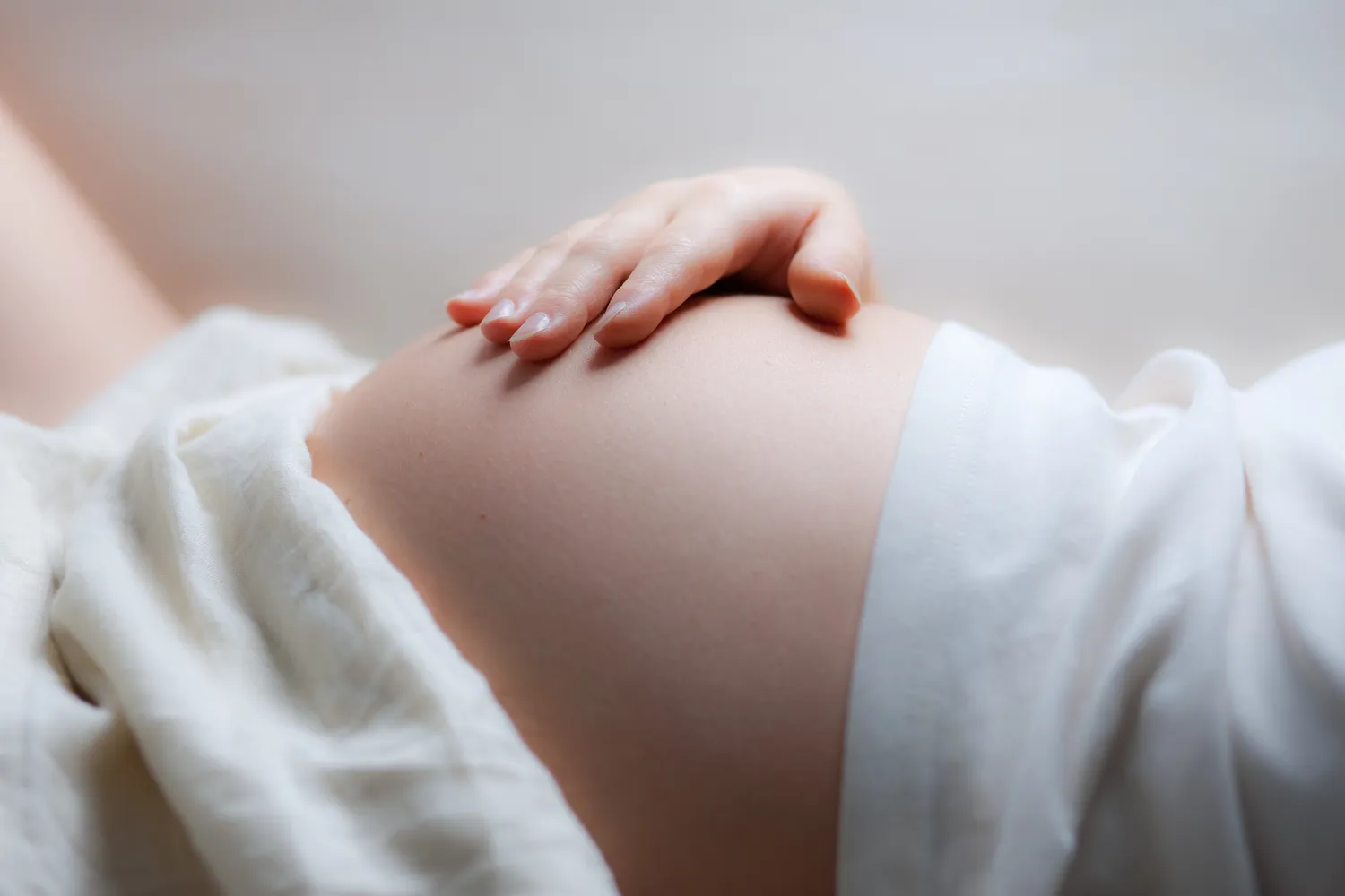 Frauenarztpraxis Dr. A. Dietrich - Gesundheitsdienste für Frauen - Nahaufnahme des Bauches einer Schwangeren, die ihre Hand darauf ruhen lässt.